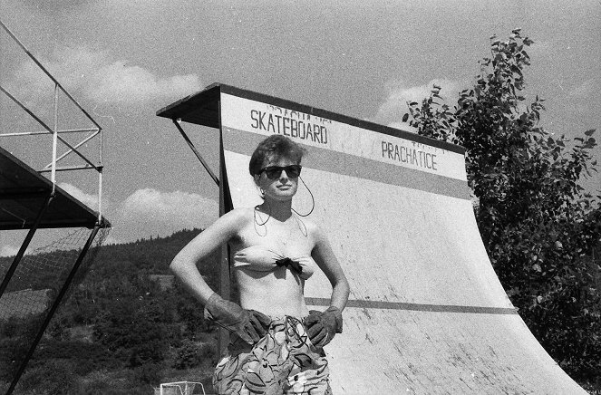 Zdjęcie; Kobieta w rękawicach i stroju kąpielowym stoi na tle rampy do skateboardingu