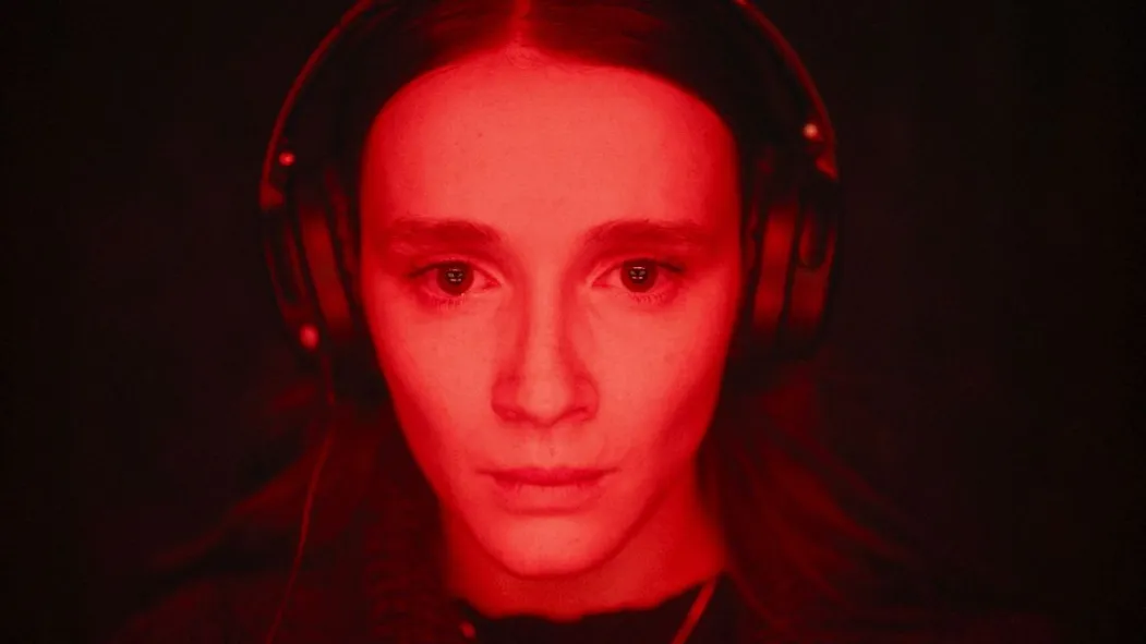 Zdjęcie; Twarz kobiety z słuchawkami na głowie oświetlona na czerwono; kobieta pustym wzrokiem patrzy przed siebie